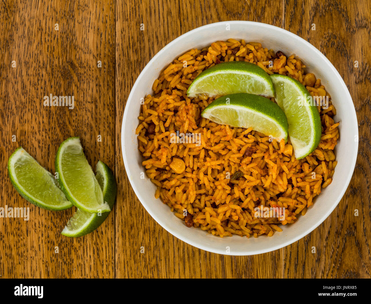 Ciotola di piccante riso messicano con lime fresco contro una quercia scura sullo sfondo di legno Foto Stock
