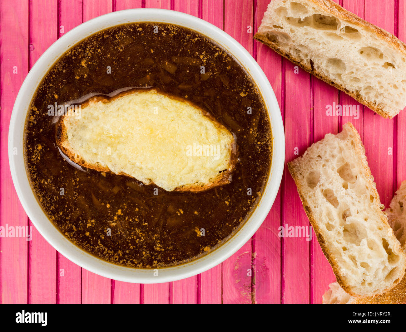 Ciotola di zuppa francese di cipolle con crostini di pane e formaggio fuso contro un di legno sfondo rosa Foto Stock