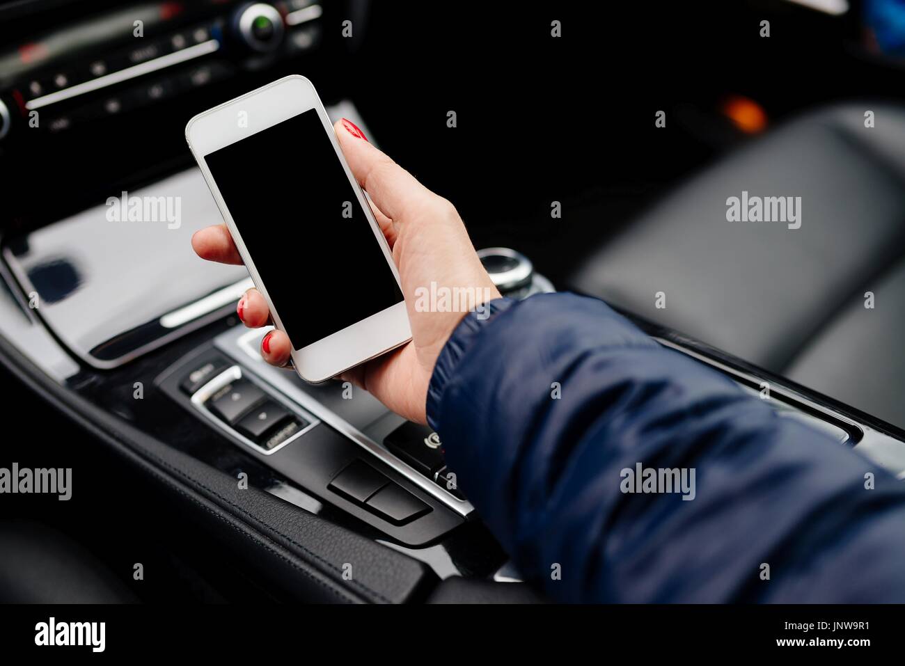 Donna che utilizza smartphone bianco in auto. Auto moderna interno Foto Stock