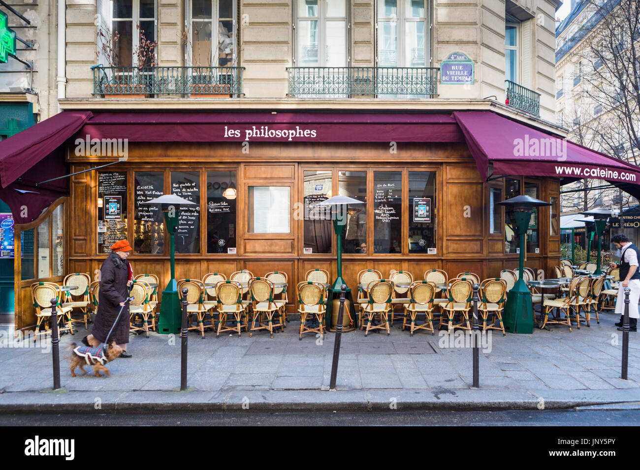 Parigi, Francia - 29 Febbraio 2016: la signora nel cappuccio arancione a piedi il suo cane passato Les Philosophes cafe su Rue Vieille du Temple nel Marais, Parigi. Foto Stock
