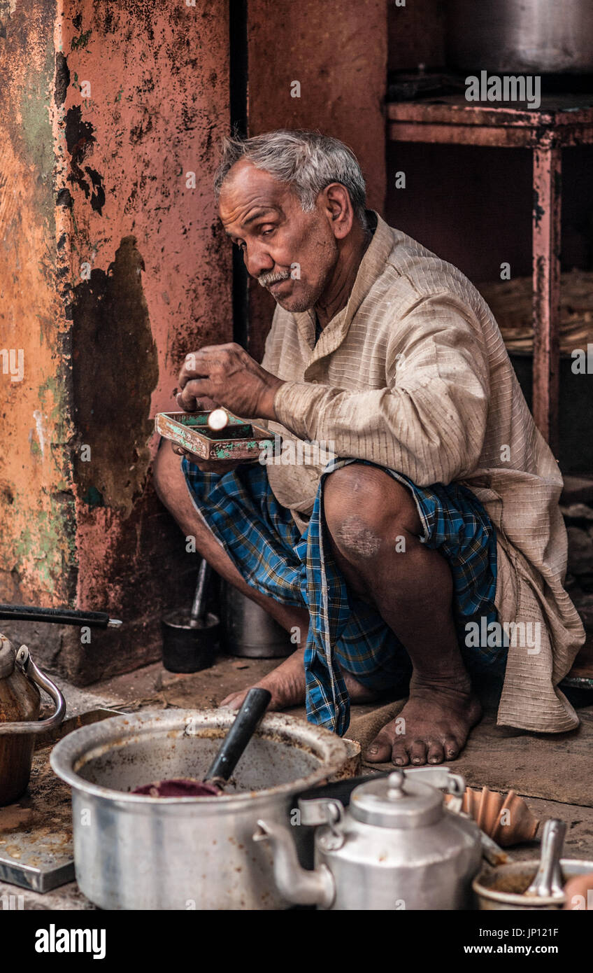 Un chai wallah siede sul suo haunches e aggiunge una moneta per il suo denaro lo stagno Foto Stock