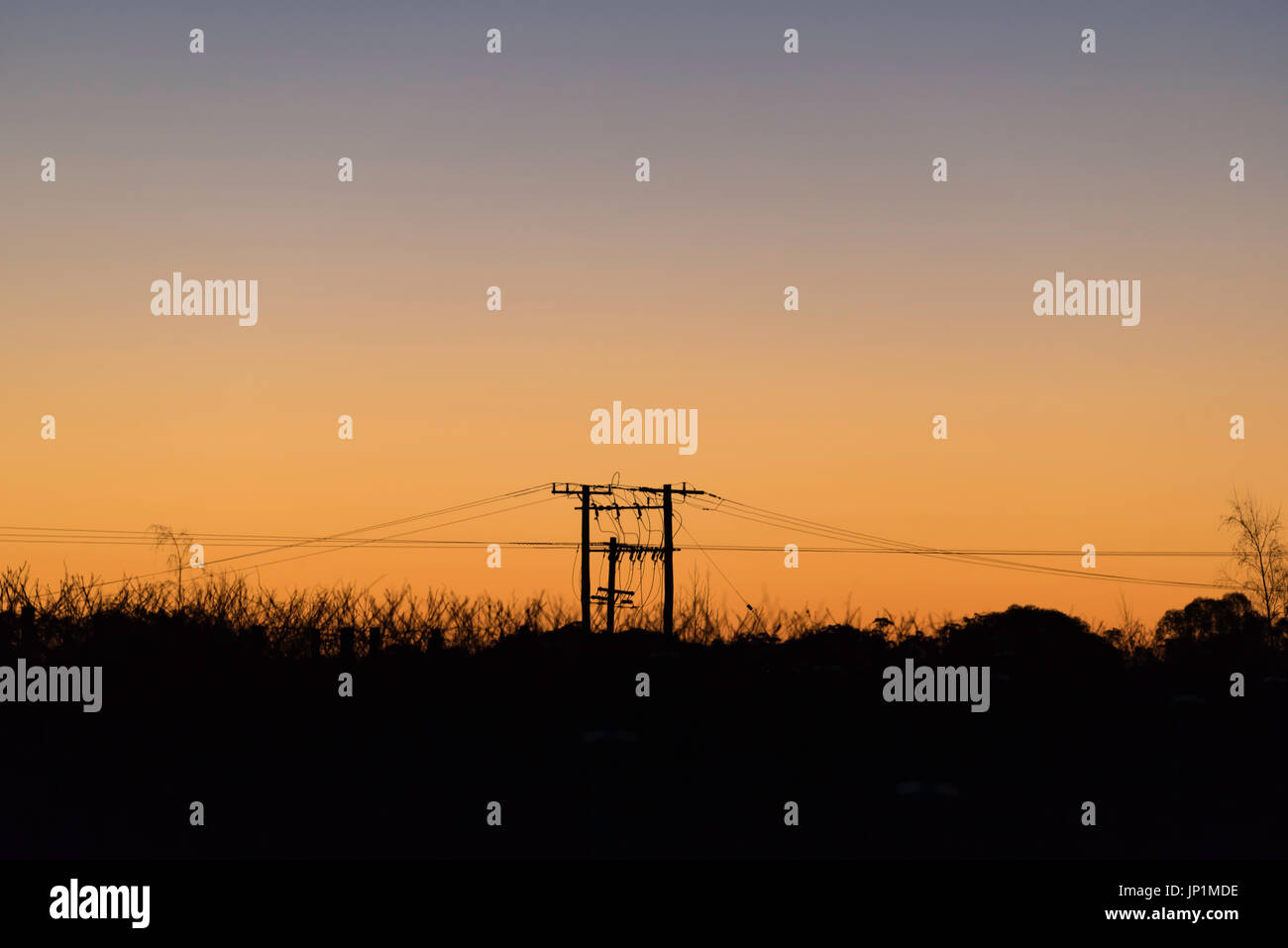 I poli di alimentazione e linee stagliano contro una luminosa arancione tramonto in western NSW, Australia Foto Stock