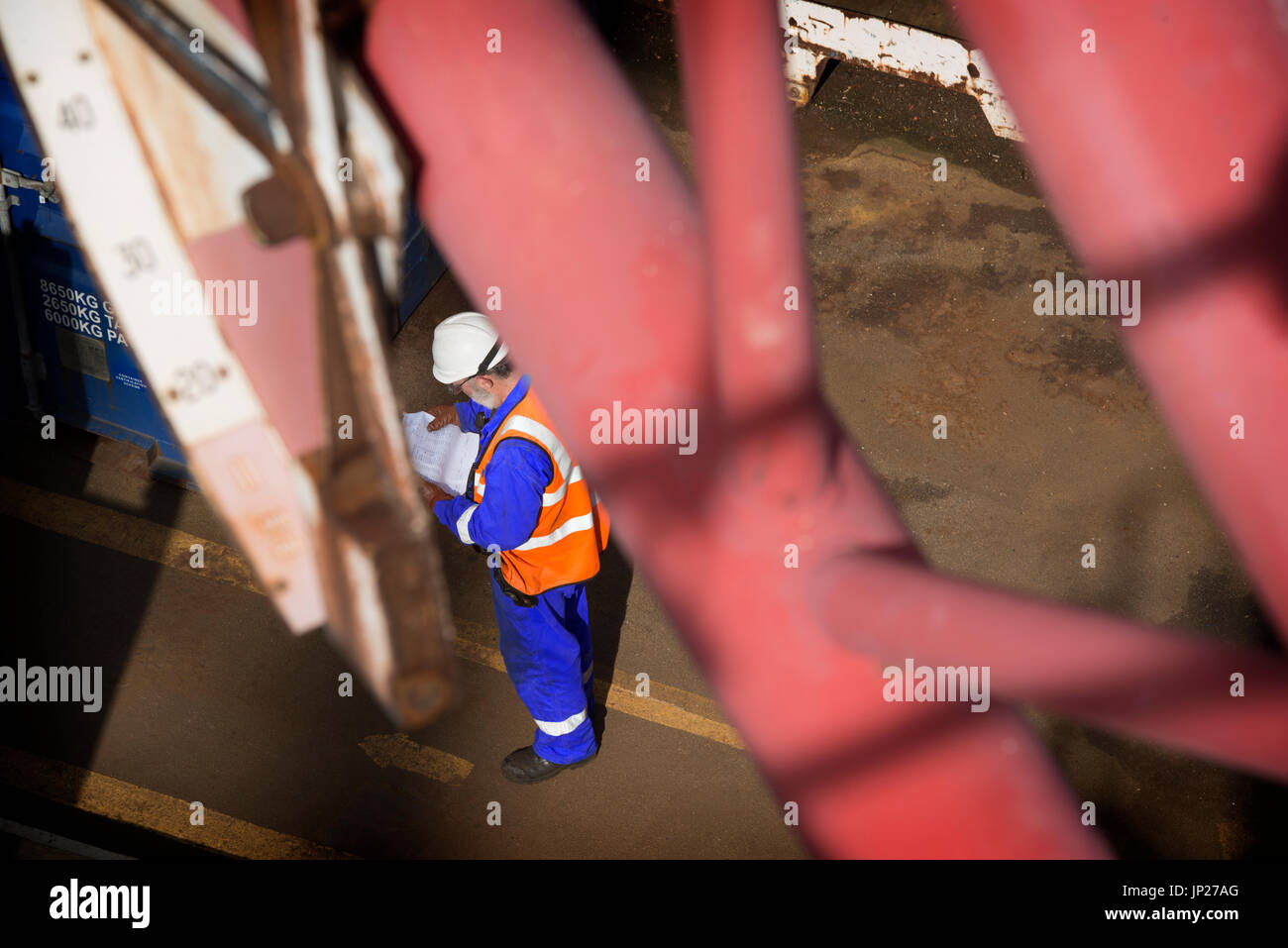 Materiali offshore coordinatore store (l'uomo) leggere il manifesto indossando tute blu / tute. Credito: lee ramsden / alamy Foto Stock