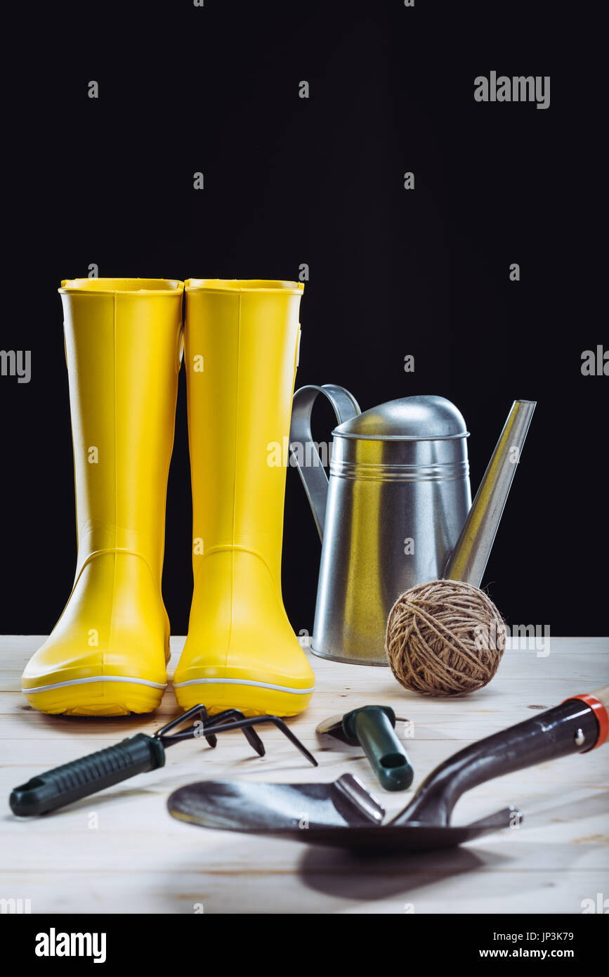 Vista ravvicinata di giallo stivali di gomma e attrezzi da giardino isolato su nero Foto Stock