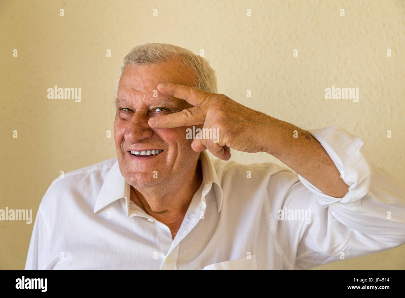 Il vecchio titolare di pensione o di rendita che mostra il gesto di roccia isolata sulla parete gialla sullo sfondo Foto Stock