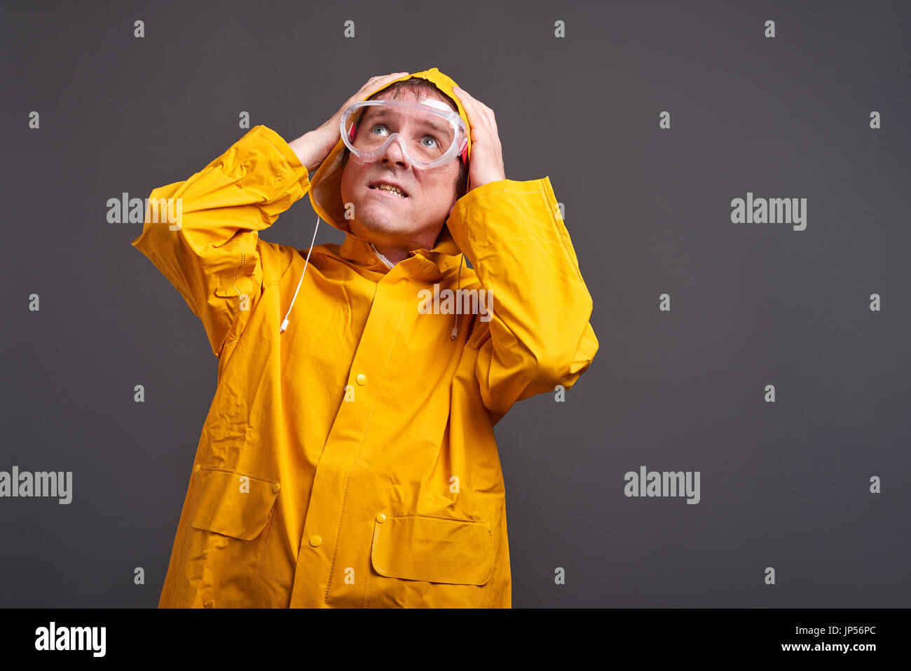 Un uomo di mezza età in un impermeabile giallo e occhiali di sicurezza sensazione di paura Foto Stock