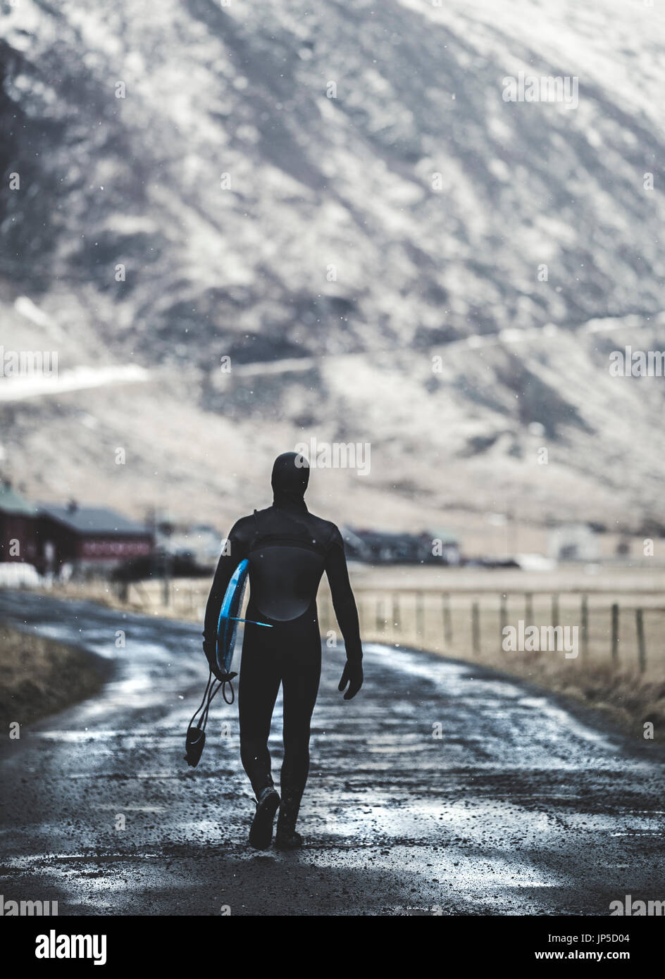 Vista posteriore di un surfista a camminare su una strada che indossa una muta e portante una tavola da surf. Foto Stock