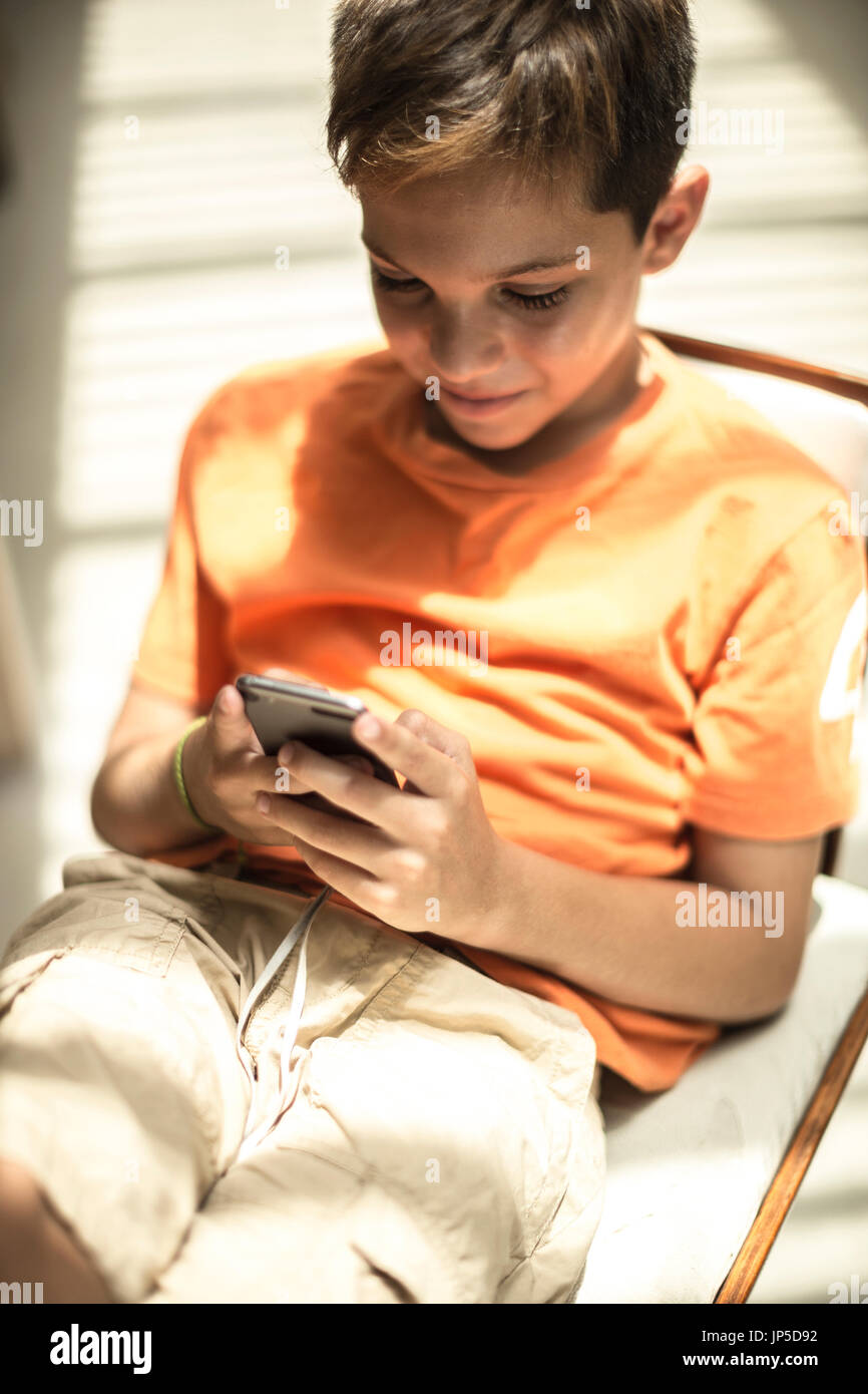 Un ragazzo seduto guardando un telefono cellulare schermo. Foto Stock