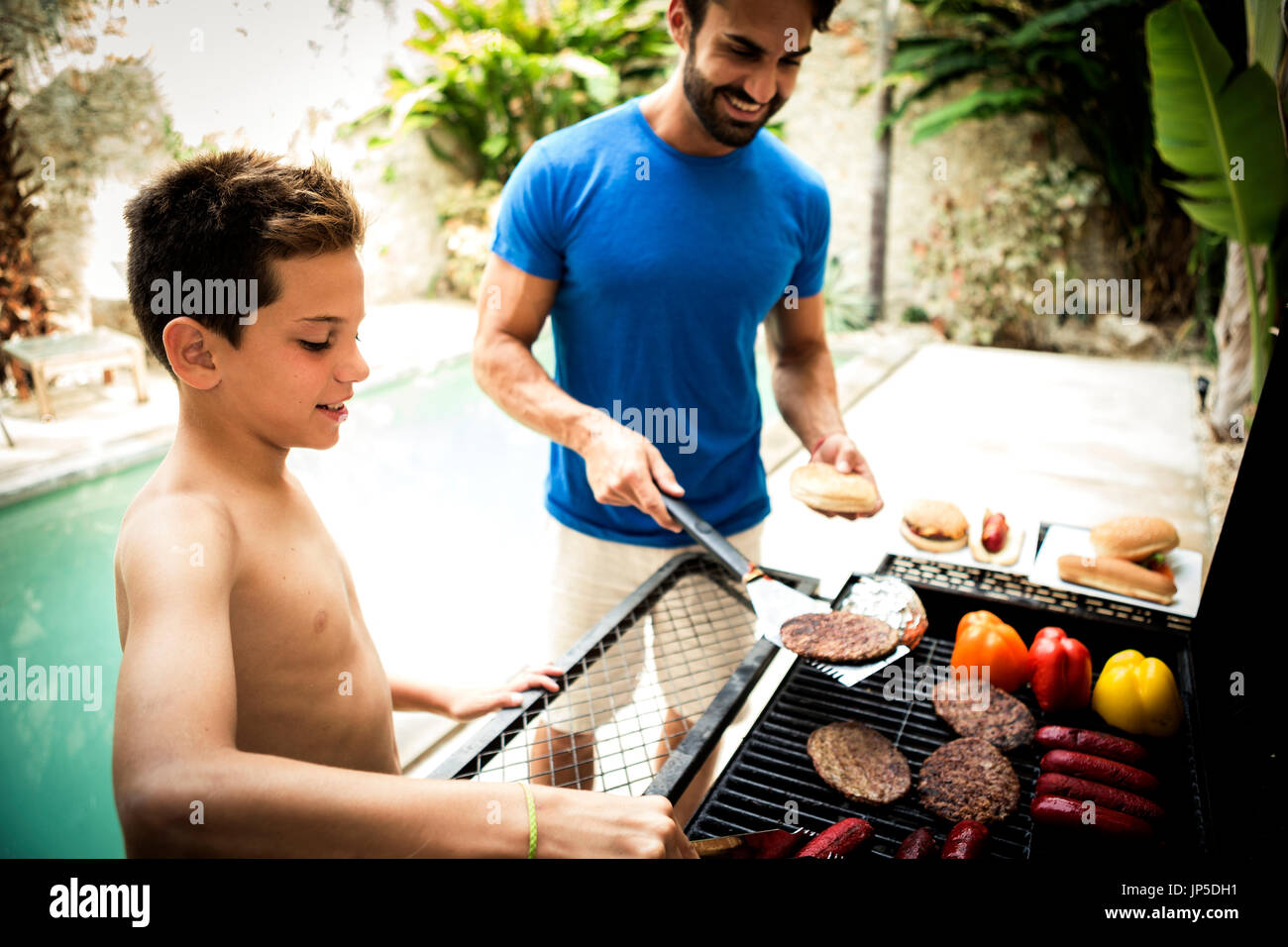 Un uomo e il ragazzo accanto a un barbecue per la cottura del cibo. Foto Stock