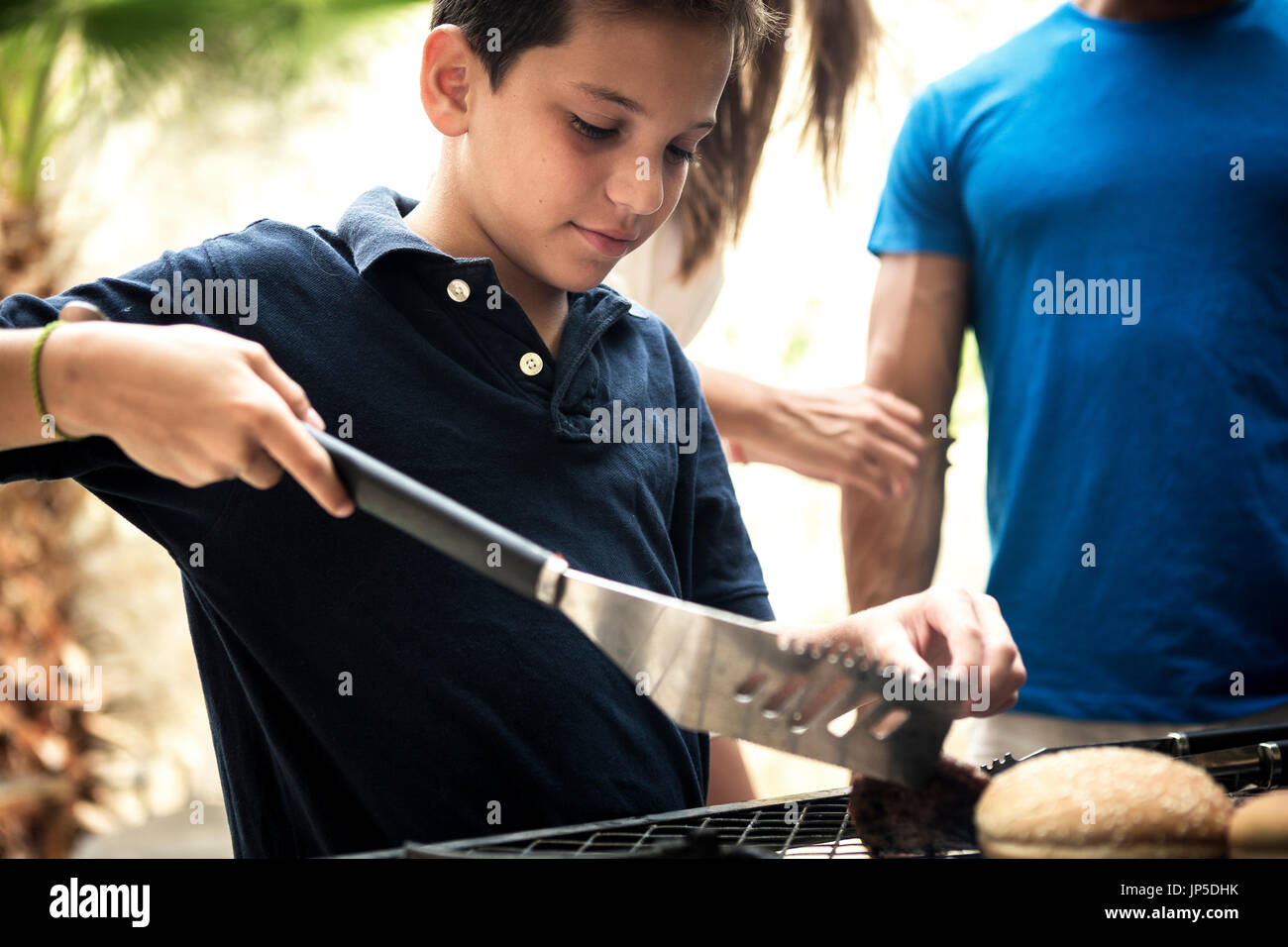 Un ragazzo tenendo le tenaglie e girando il cibo su un barbecue. Foto Stock