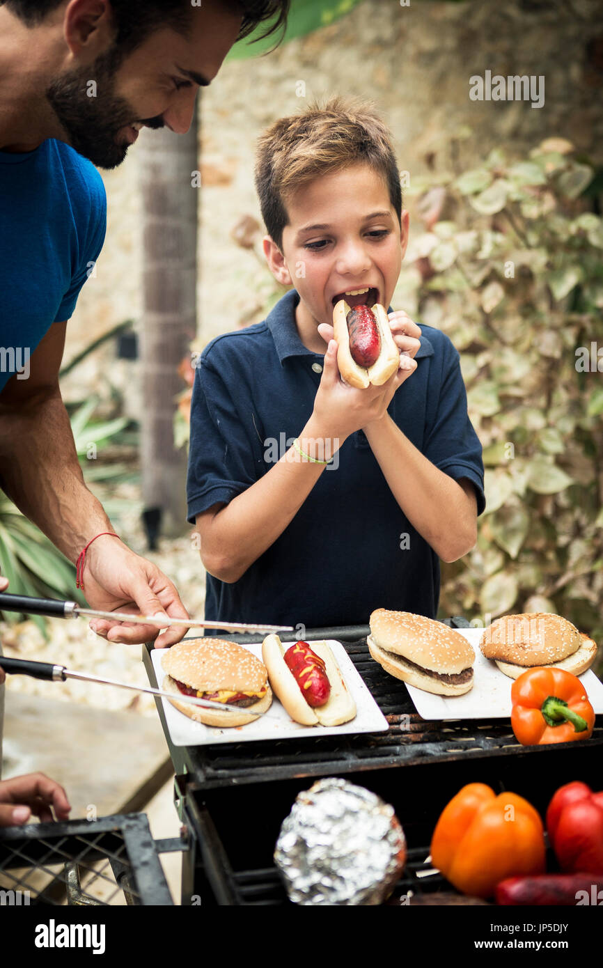 Un ragazzo e un uomo in piedi in un aperto barbecue per mangiare. Foto Stock