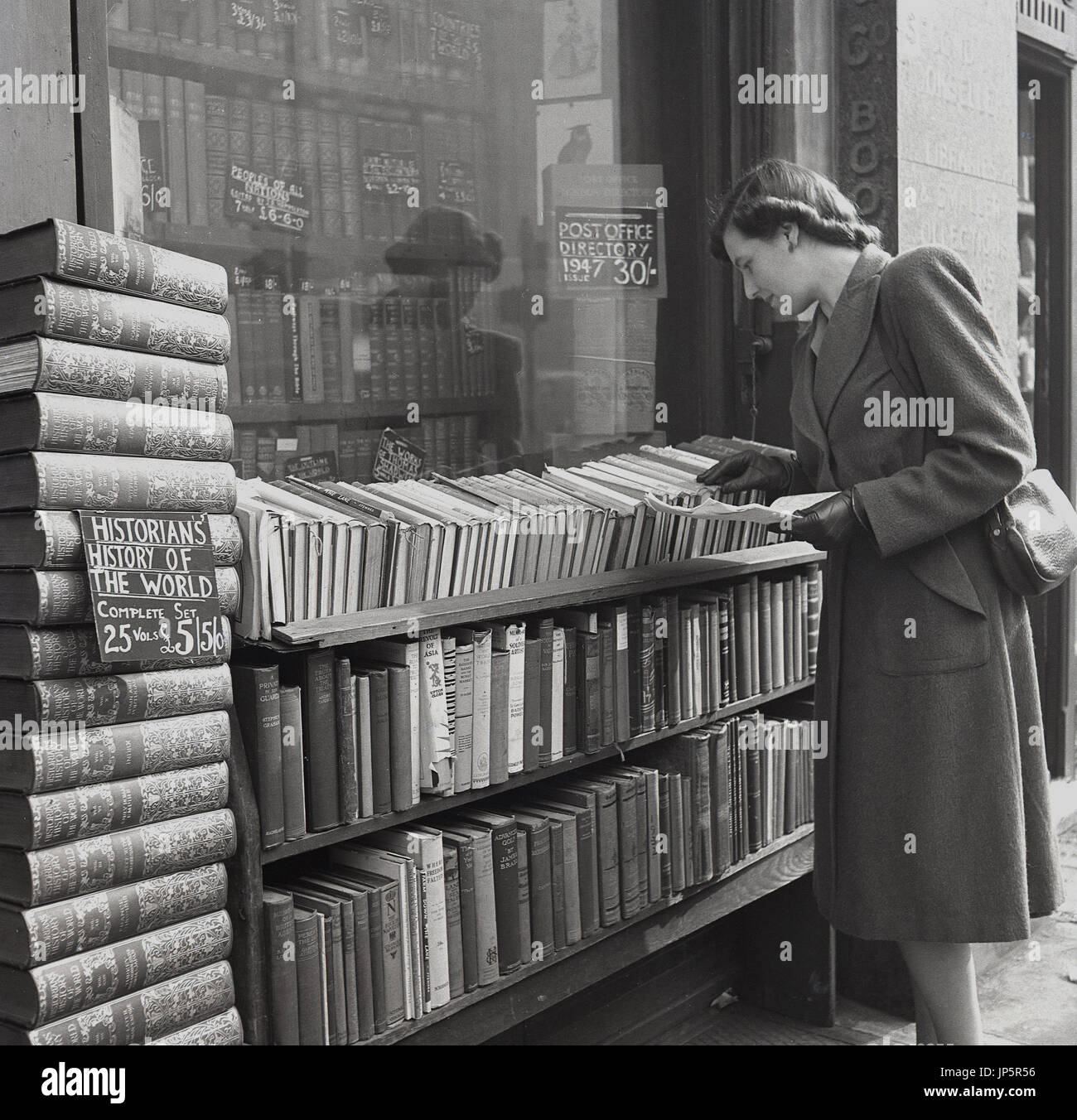 1948, storico, Inghilterra, Charing Cross Rd, London, una giovane signora esplora le righe di seconda mano libri hardback impilati al di fuori di una libreria antiquaria. Foto Stock