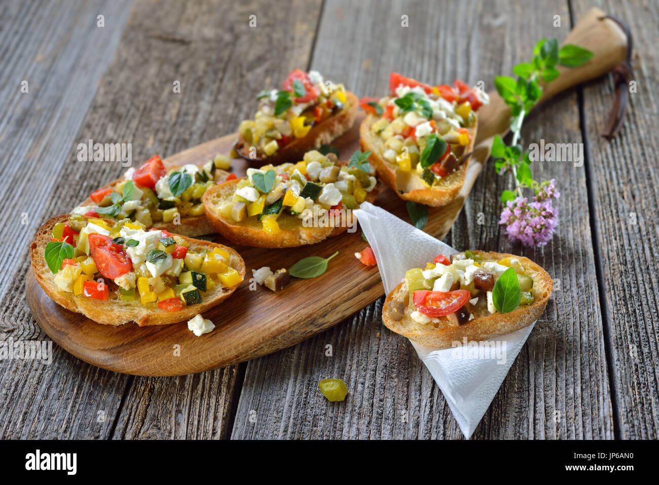 Vegetariani caldi crostini: crostini al forno con misto di verdure greca con il formaggio feta servita su un tagliere di legno Foto Stock
