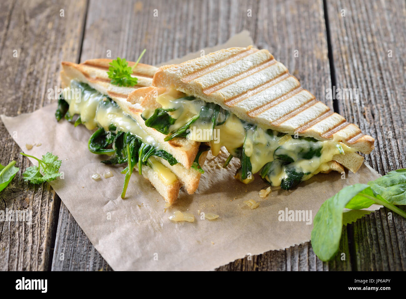 Premuto vegetariano panini doppia con giovani foglie di spinaci, cipolle e formaggio servita su carta a sandwich su un tavolo di legno Foto Stock