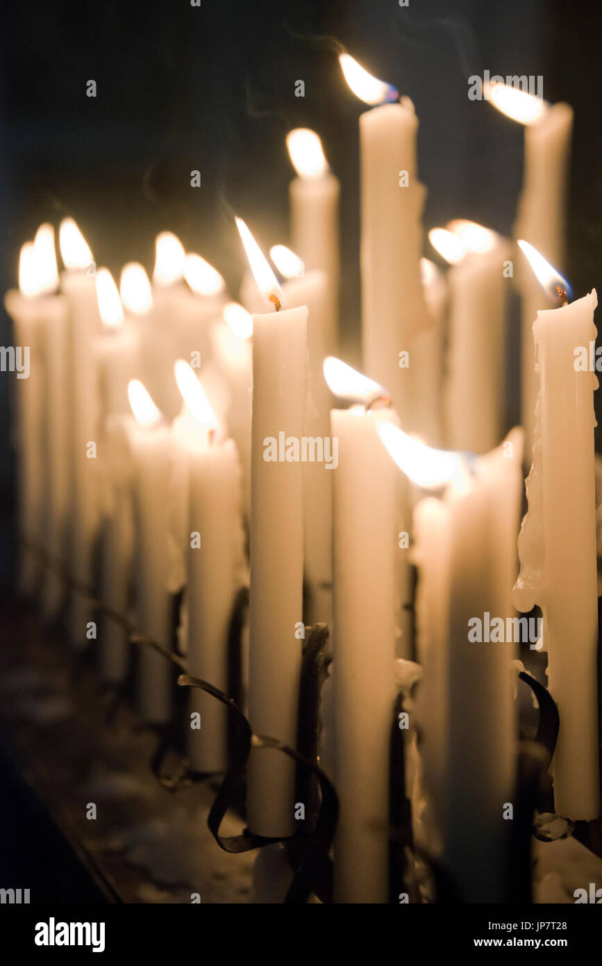 Verticale di chiusura del file di candele votive a bruciare in una chiesa. Foto Stock