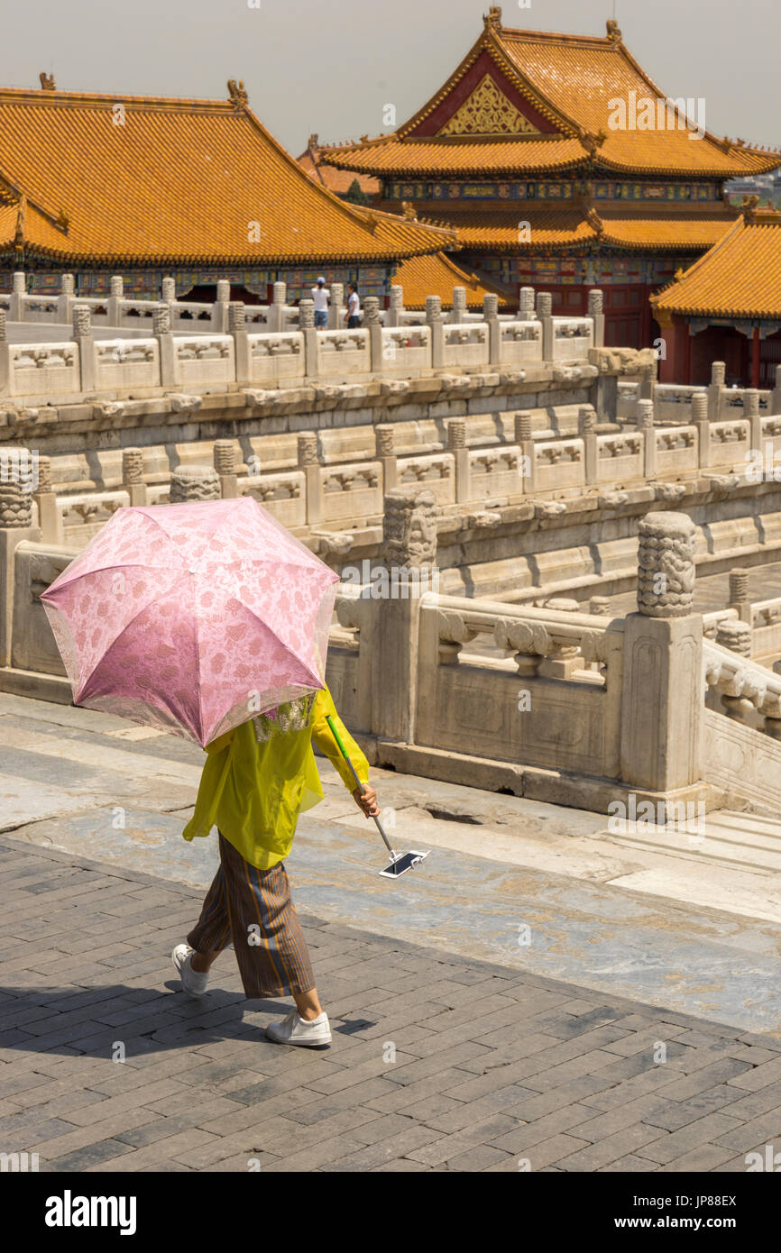 Donna che mantiene ombra ombrello e telefono cellulare con selfie stick a piedi dal palazzo della purezza Celeste alla Città Proibita di Pechino Foto Stock