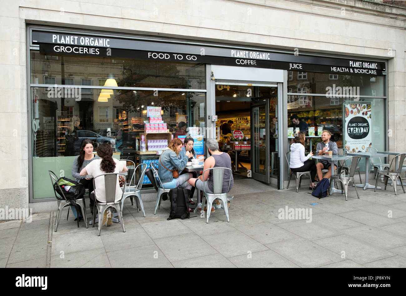 La gente seduta a mangiare a bere a tavoli fuori pianeta supermercato organico store su Essex Road a Londra N1 UK KATHY DEWITT Foto Stock