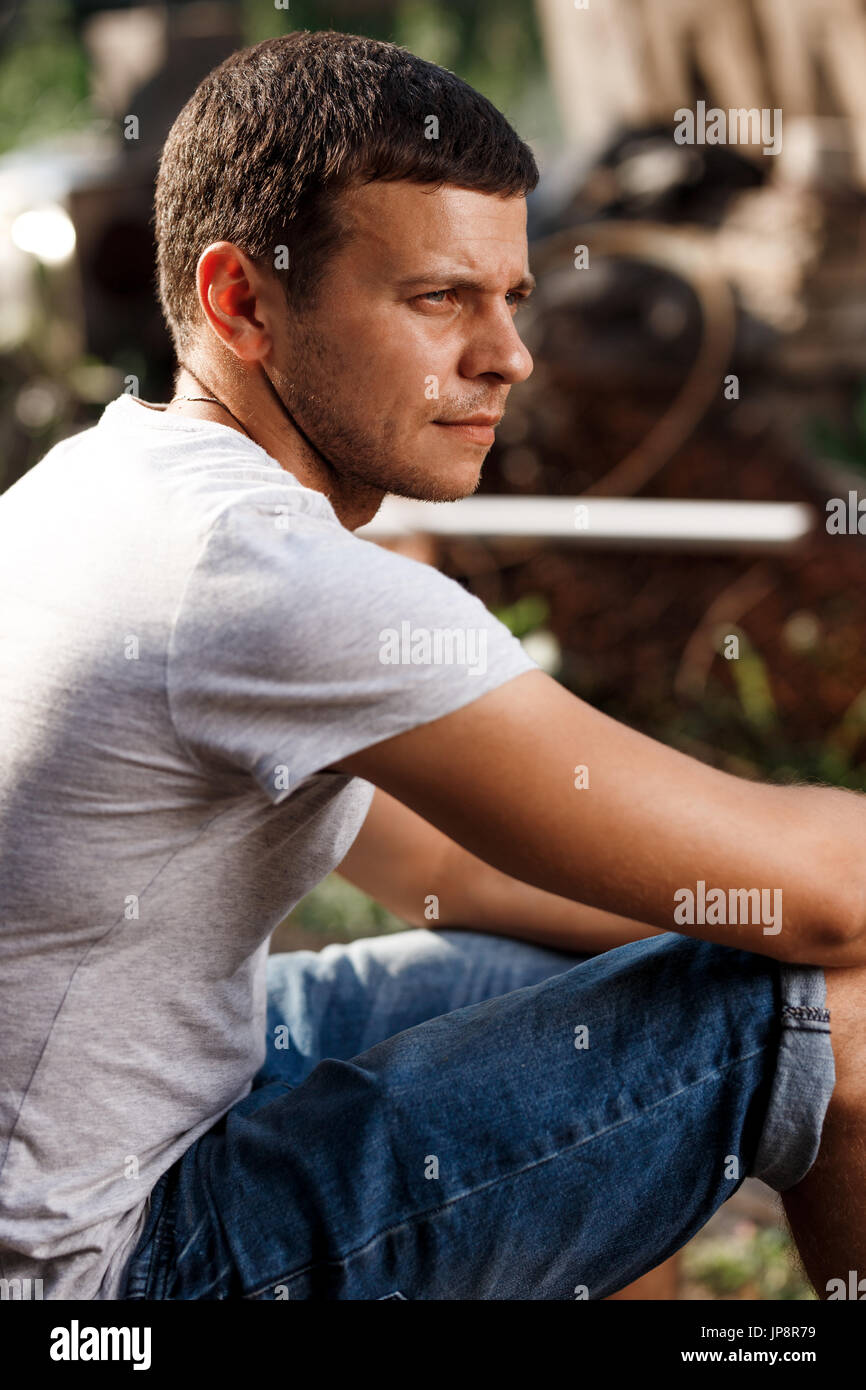 Outdoor ritratto di un bel giovane uomo in jeans e maglietta a maniche corte grigia. Foto Stock