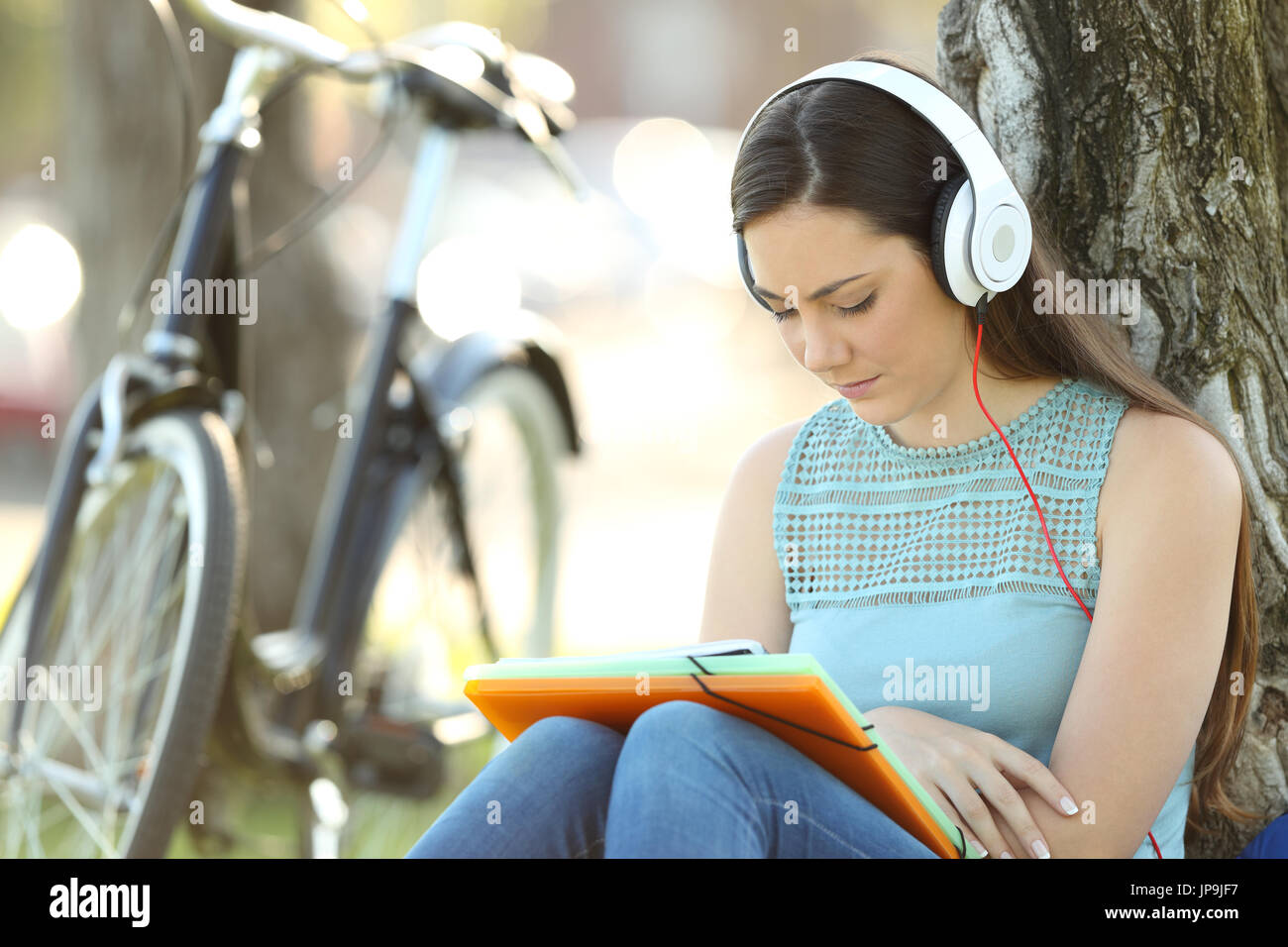 Del singolo studente indossando le cuffie audizione di apprendimento tutorials audio seduto in un parco Foto Stock