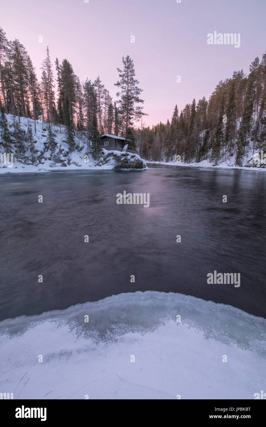 Una capanna in legno circondato dal fiume congelato e boschi innevati al crepuscolo Juuma Myllykoski Lapponia Regione Finlandia Europa Foto Stock