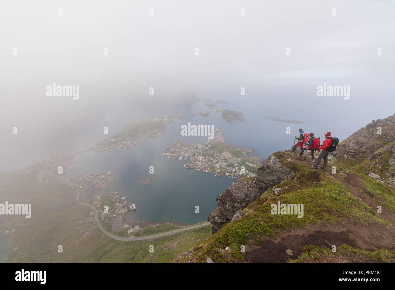 Gli escursionisti sulla sommità del picco roccioso ammirare il blu del mare circondato da nebbia Moskenes Reinebringen Isole Lofoten in Norvegia Europa Foto Stock