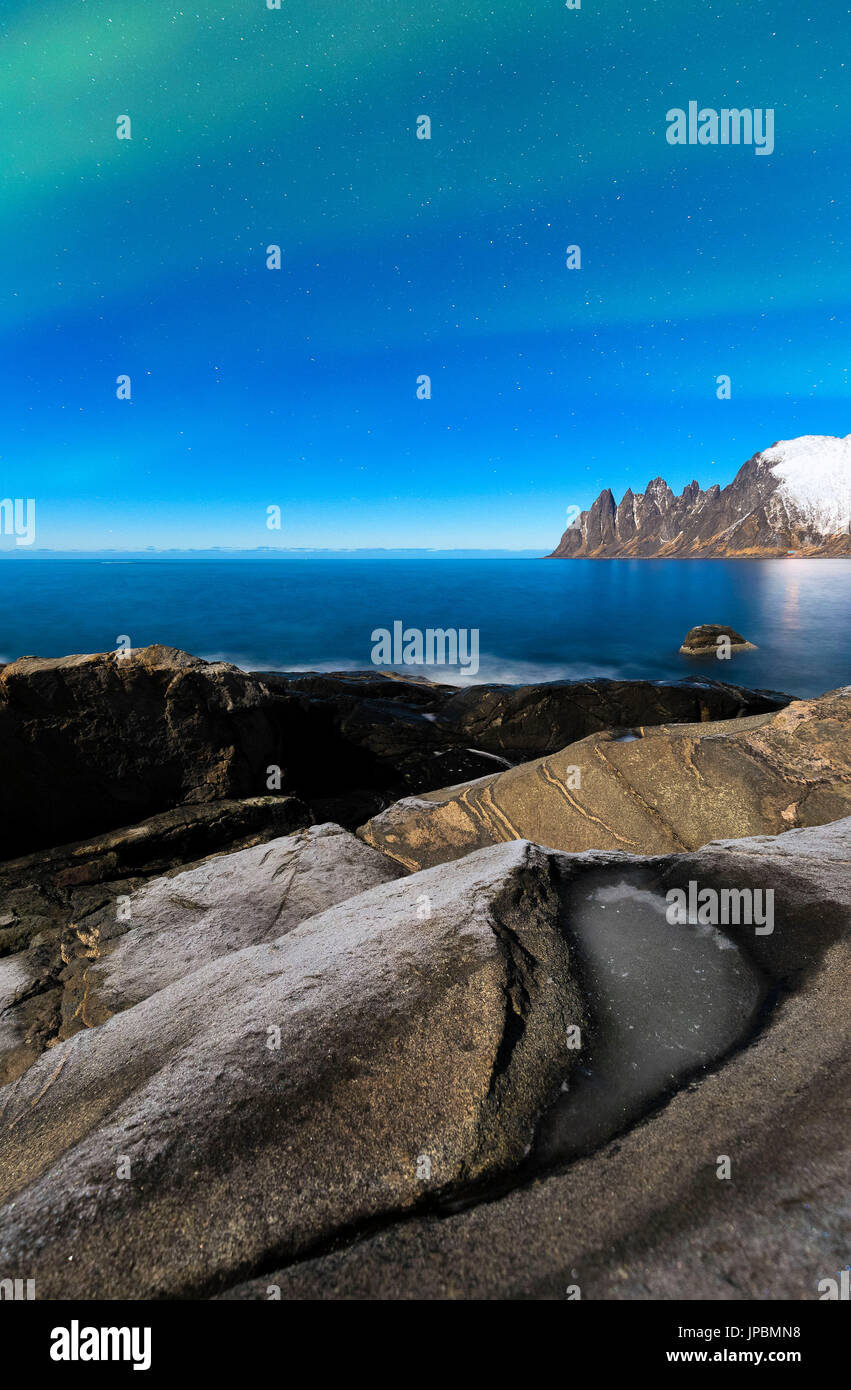 Luci del Nord al di sopra della baia con moonlight che illumininates rock di Tungeneset. Tungeneset, Ersfjorden, Senja, Norvegia, l'Europa. Foto Stock
