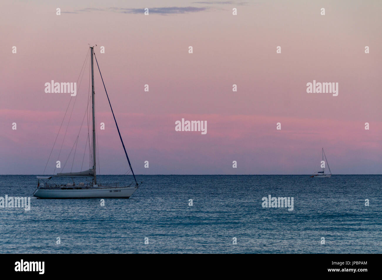 Due barche a vela vela sul mare calmo vicino alla costa sud della Sardegna al tramonto. Mare Mediterraneo, Italia Foto Stock