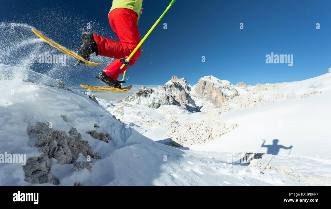 Un escursionista con le racchette da neve giallo salta fuori il boulder con la pala del gruppo in background, provincia di Trento, Trentino Alto Adige, Italia, Europa Foto Stock