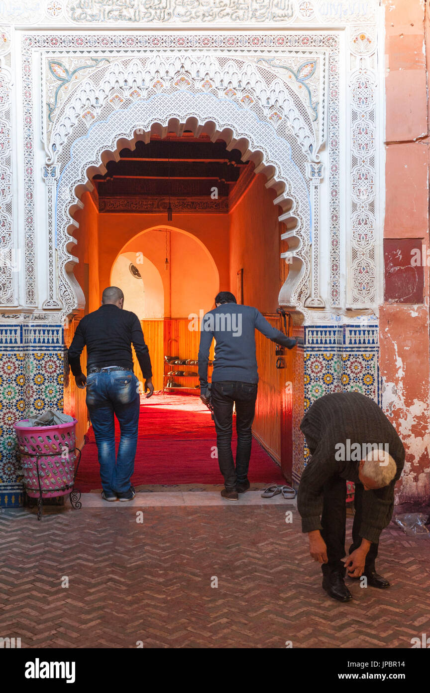 Marrakech, Marocco. Gli uomini di decollare le loro scarpe all'ingresso di una moschea. Foto Stock