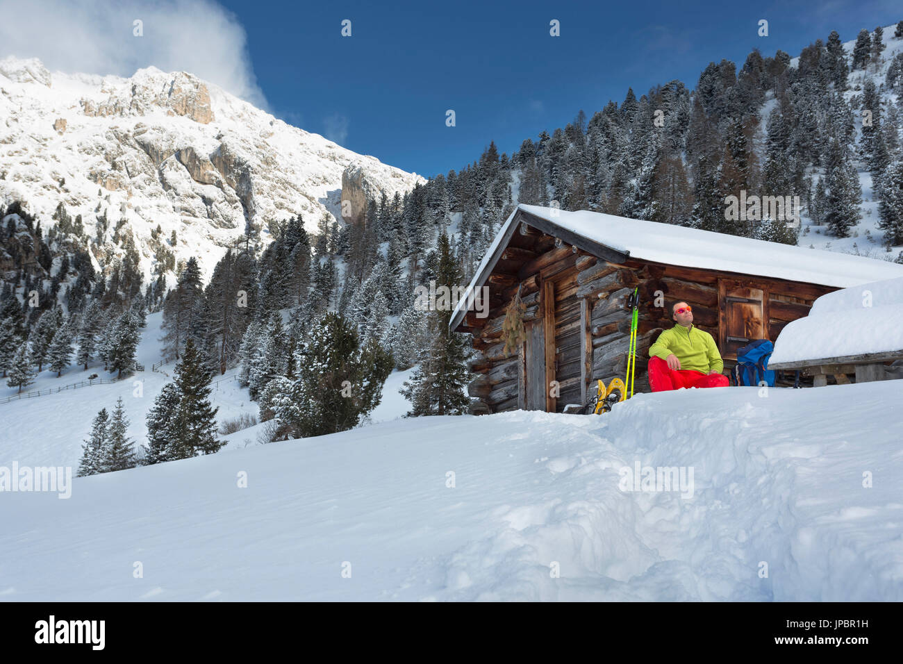 Un inverno escursioni con le racchette da neve nel Puez Geisler parco naturale con una persona seduta da una vecchia capanna e guardando verso i monti della provincia di Bolzano, Alto Adige, Trentino Alto Adige, Italia, Europa Foto Stock