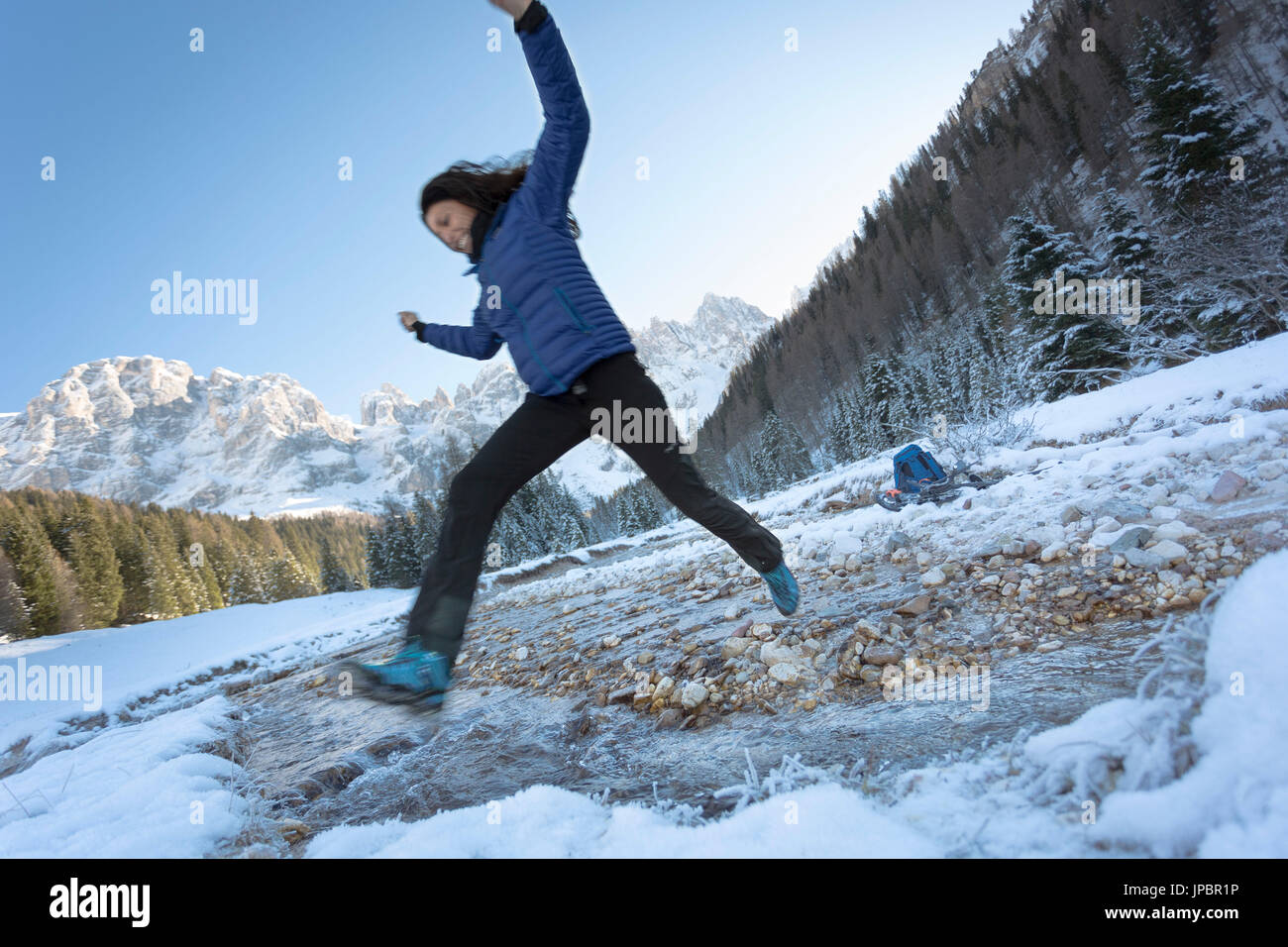 Un gioioso momento durante un trekking invernale mentre il modello salta il creek in Val Venegia, in provincia di Trento, Trentino, Italia, Europa Foto Stock