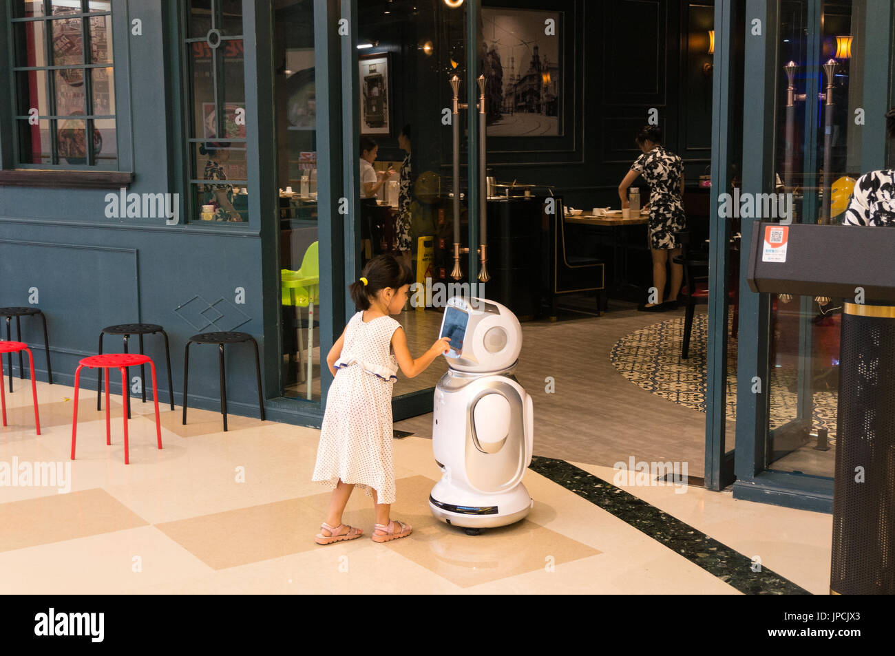 Ragazza giovane toccando del robot nella faccia anteriore del ristorante a Shenzhen, Cina Foto Stock