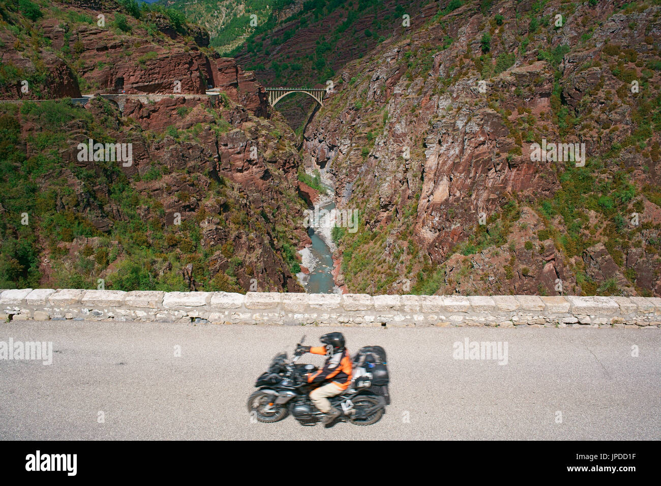 Motociclista (con motion blur) che guida su una strada scogliera sopra il fiume Var, Ponte della sposa in lontananza. Guadaluis Gorge, Francia. Foto Stock