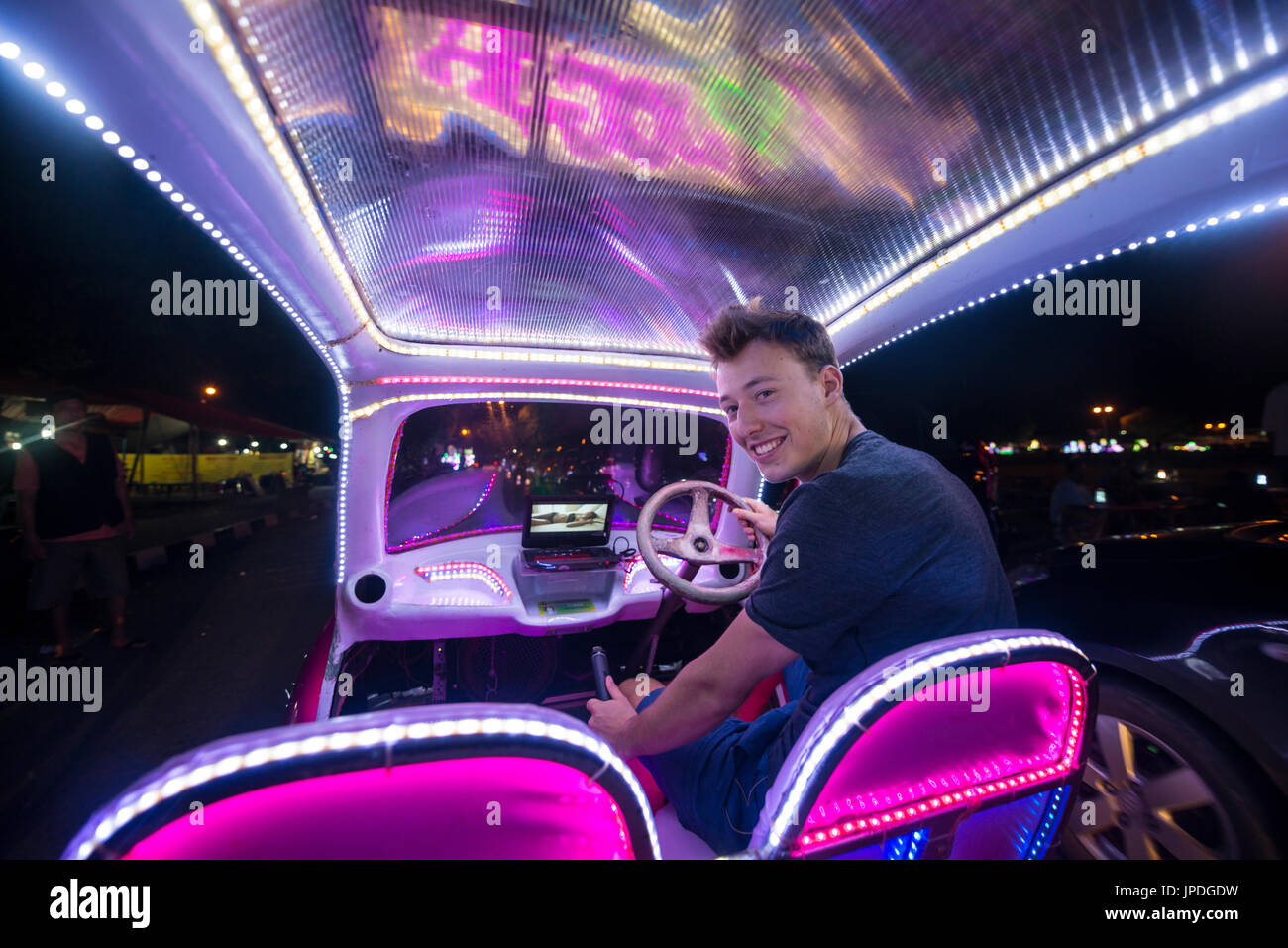 Giovane uomo alla guida di una vettura colorati illuminato con LED, pedale auto, Yogyakarta, Java, Indonesia Foto Stock