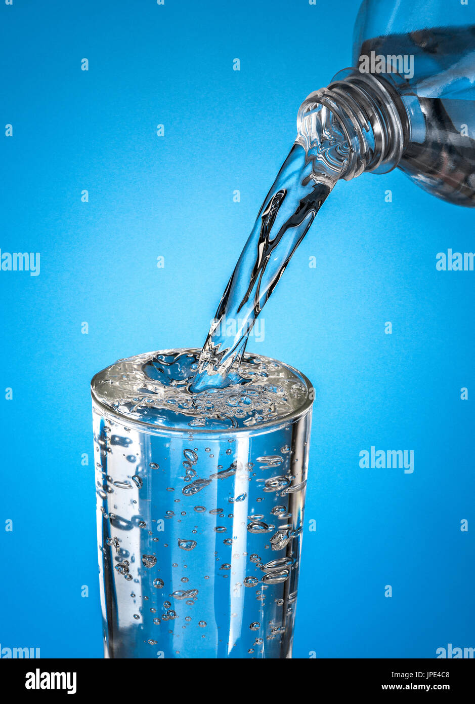 Versare acqua in un bicchiere su sfondo blu Foto Stock