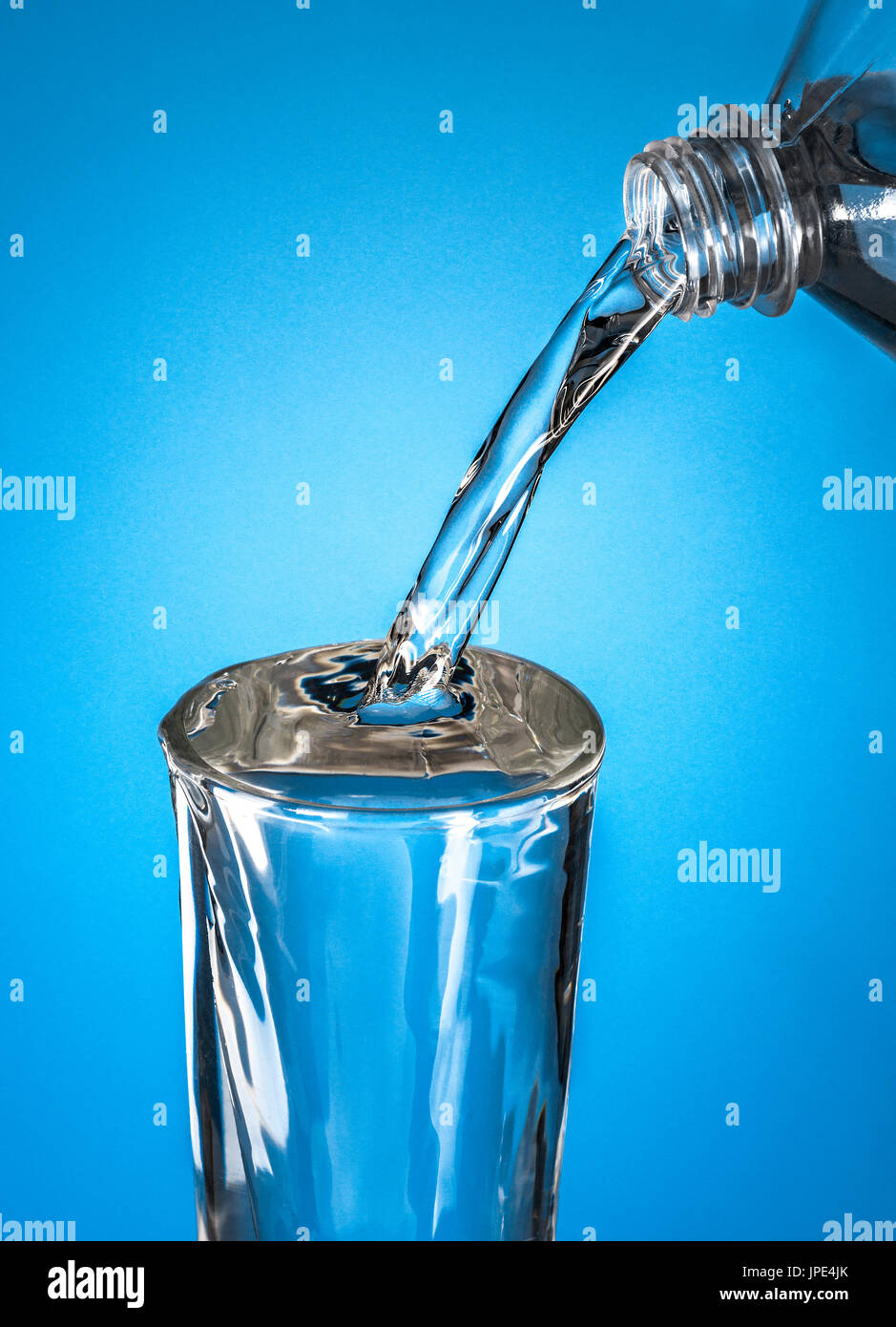 Bottiglia di acqua versando in vetro su sfondo blu Foto Stock