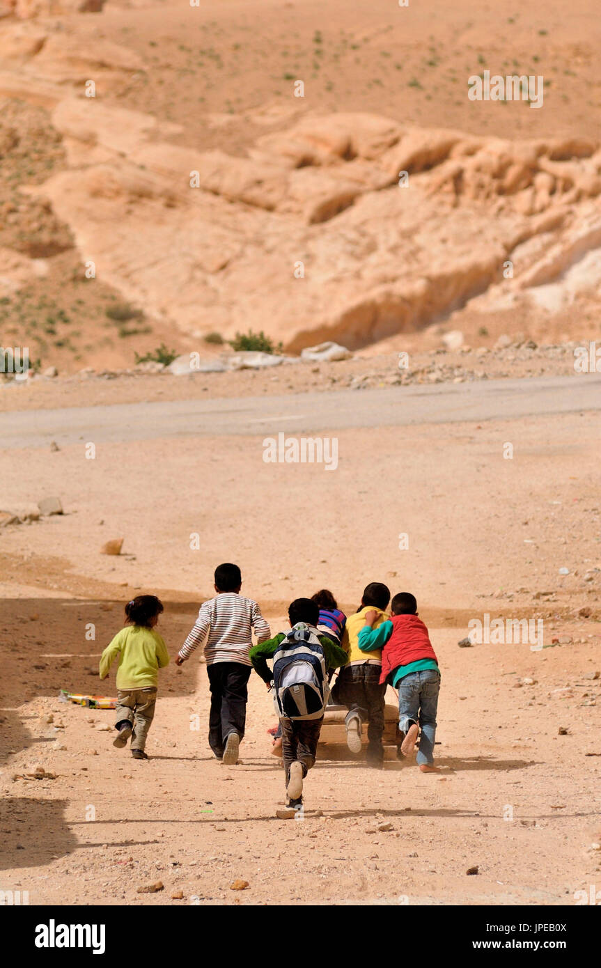 Bambini che giocano a caccia di un carrello costruito da se stesso, su una strada polverosa nella periferia di Petra, Giordania Foto Stock