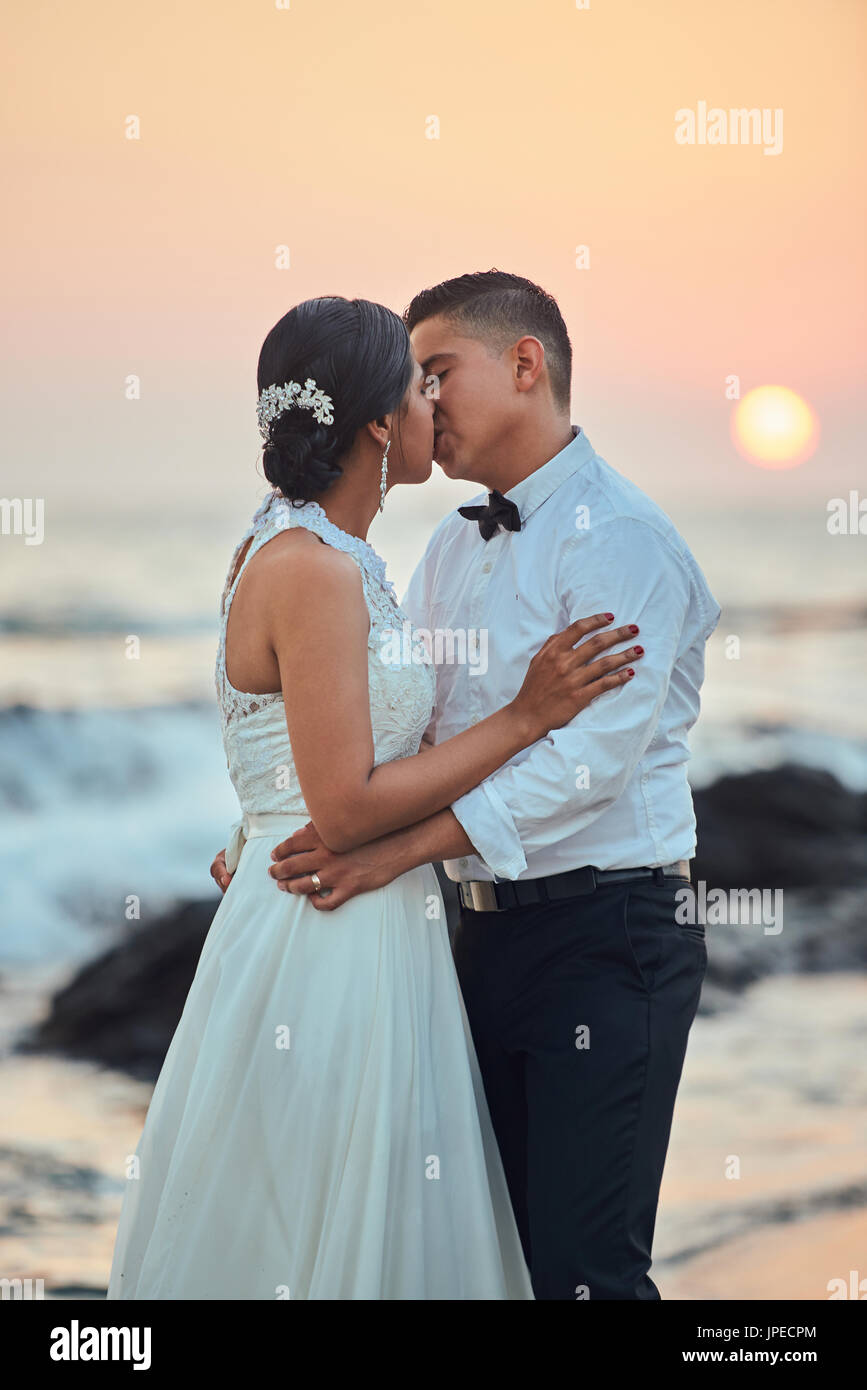 Coppie in viaggio di nozze baciare sulla spiaggia al tramonto del tempo. Sposa e lo sposo kiss Foto Stock