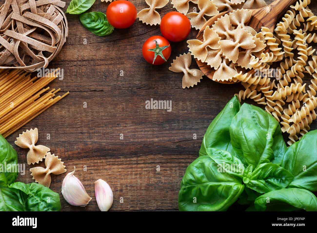 Cucina Italiana concetto - Varietà di pasta integrale con basilico fresco, pomodoro e aglio su legno rustico sfondo. Vista aerea con spazio di copia Foto Stock