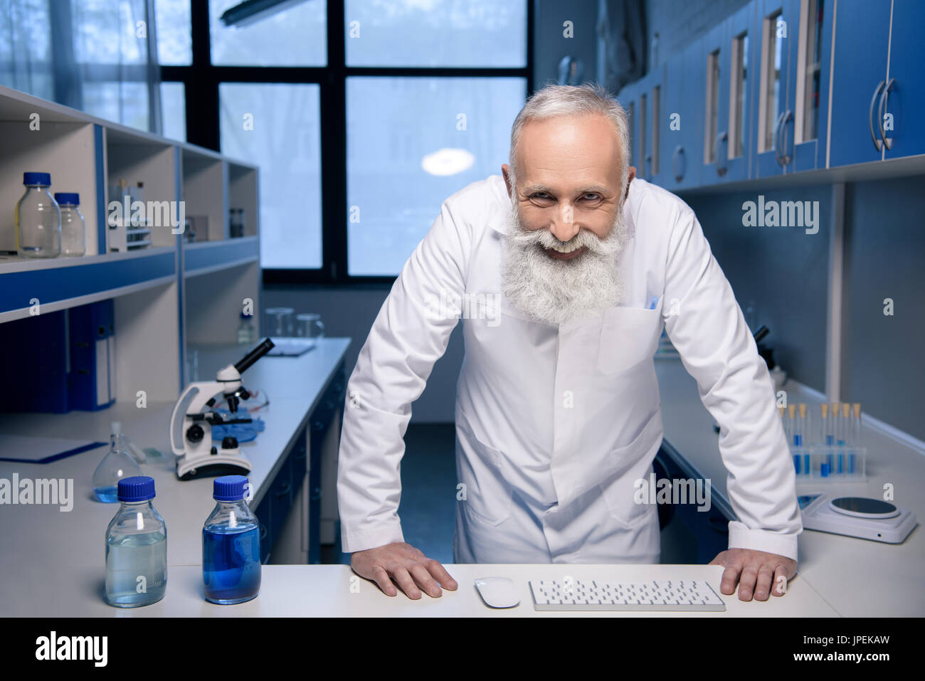 Ritratto di uno scienziato sorridente con le mani sul tavolo guardando la fotocamera in laboratorio Foto Stock Ritratto di uno scienziato sorridente con le mani sul tavolo guardando la fotocamera in laboratorio Foto Stock