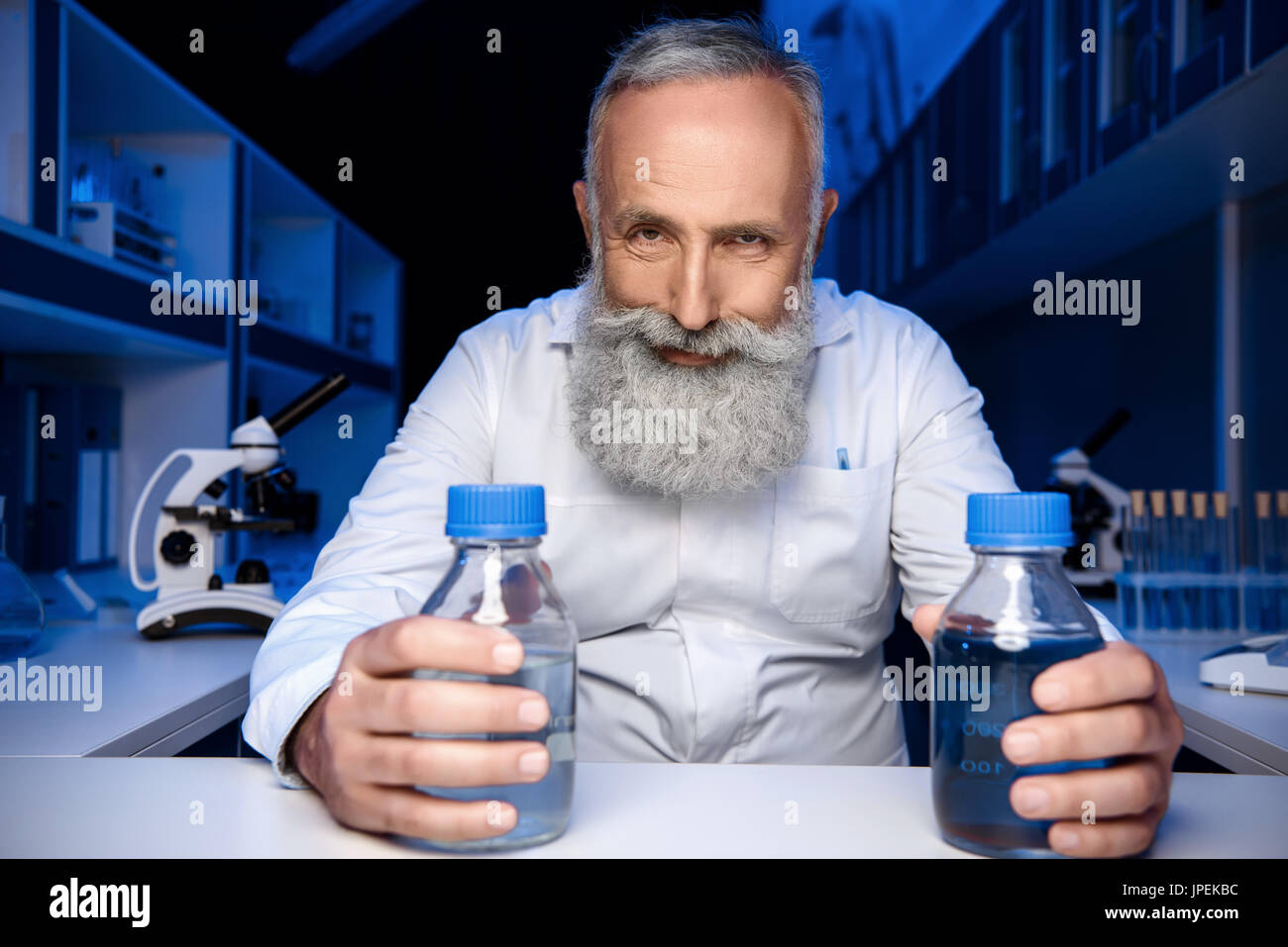 Ritratto di astuzia scienziato tenendo le bottiglie con reagenti e guardando la telecamera in laboratorio Foto Stock