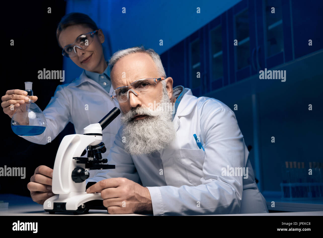 Scienziato usando microscopio mentre si collega il reagente di contenimento nel tubo in laboratorio Foto Stock