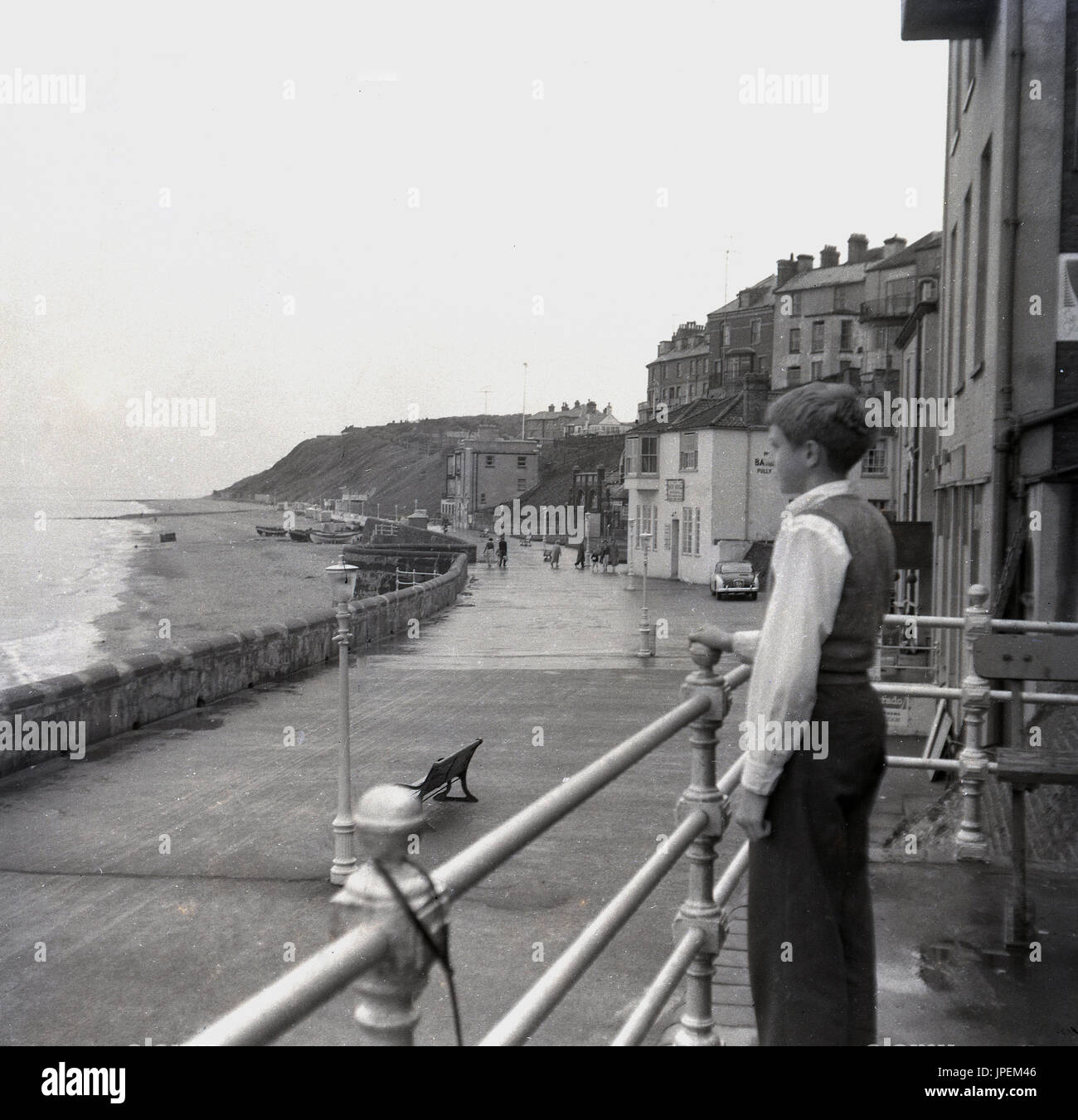 Fine degli anni quaranta, giovane ragazzo si erge da ringhiere che guardano sul mare e spiaggia a Cromer, Norfolk, Inghilterra. Foto Stock