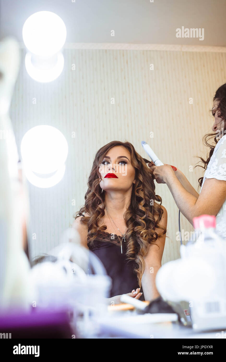 Hair stylist rendendo boccoli di brunette donna. parrucchiere lavora con bella donna capelli nel salone di parrucchiere. Foto Stock