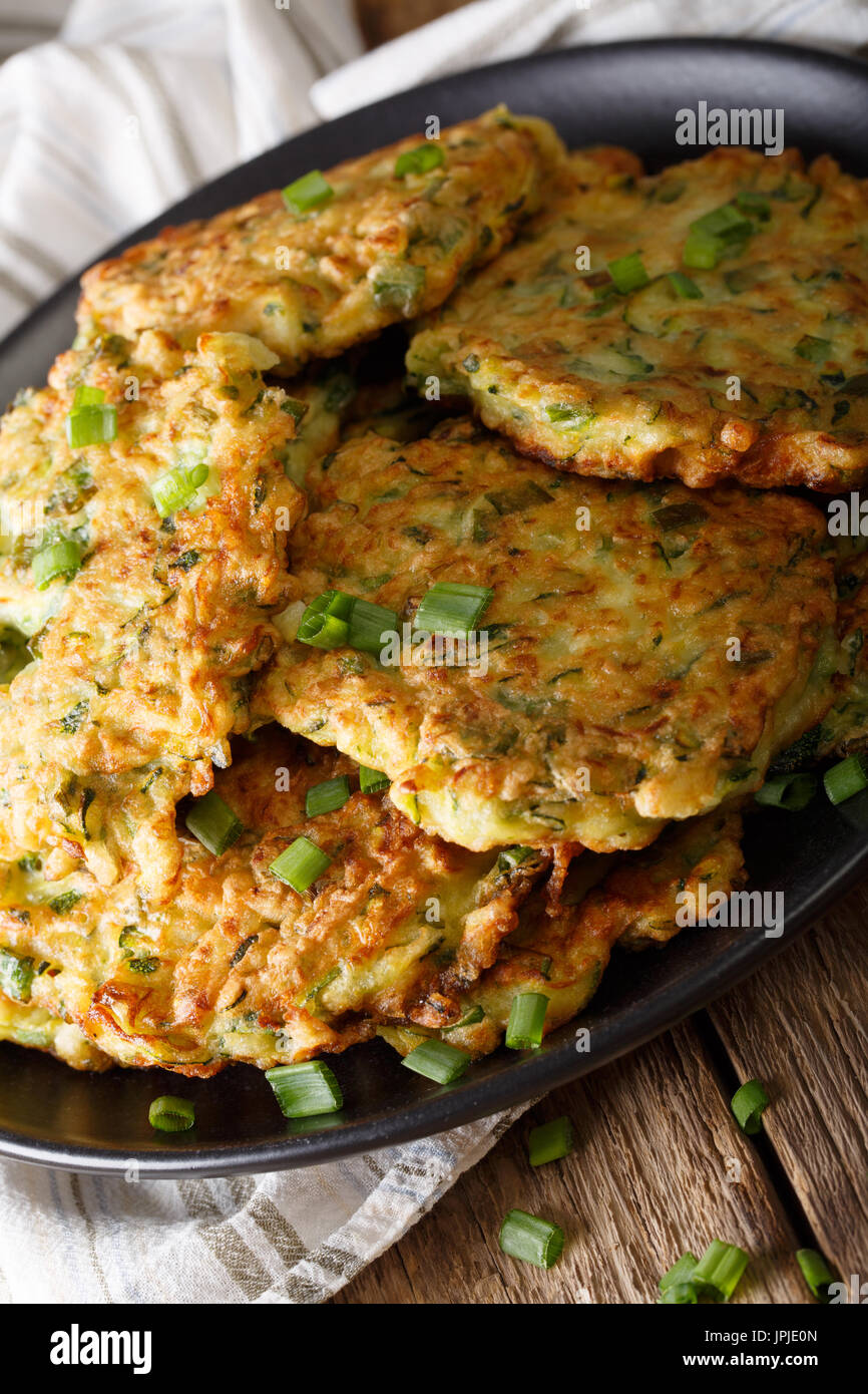 Frittelle di zucchini con cipolla verde su una piastra di close-up su una tavola verticale. Foto Stock