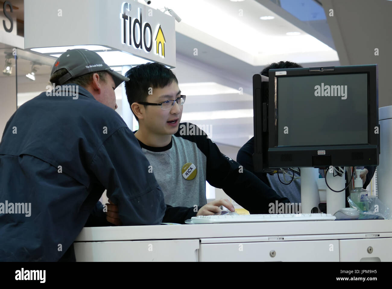 Persone che chiedono fido addetto alle vendite su cellulare all'interno del piano Burnaby shopping mall Foto Stock