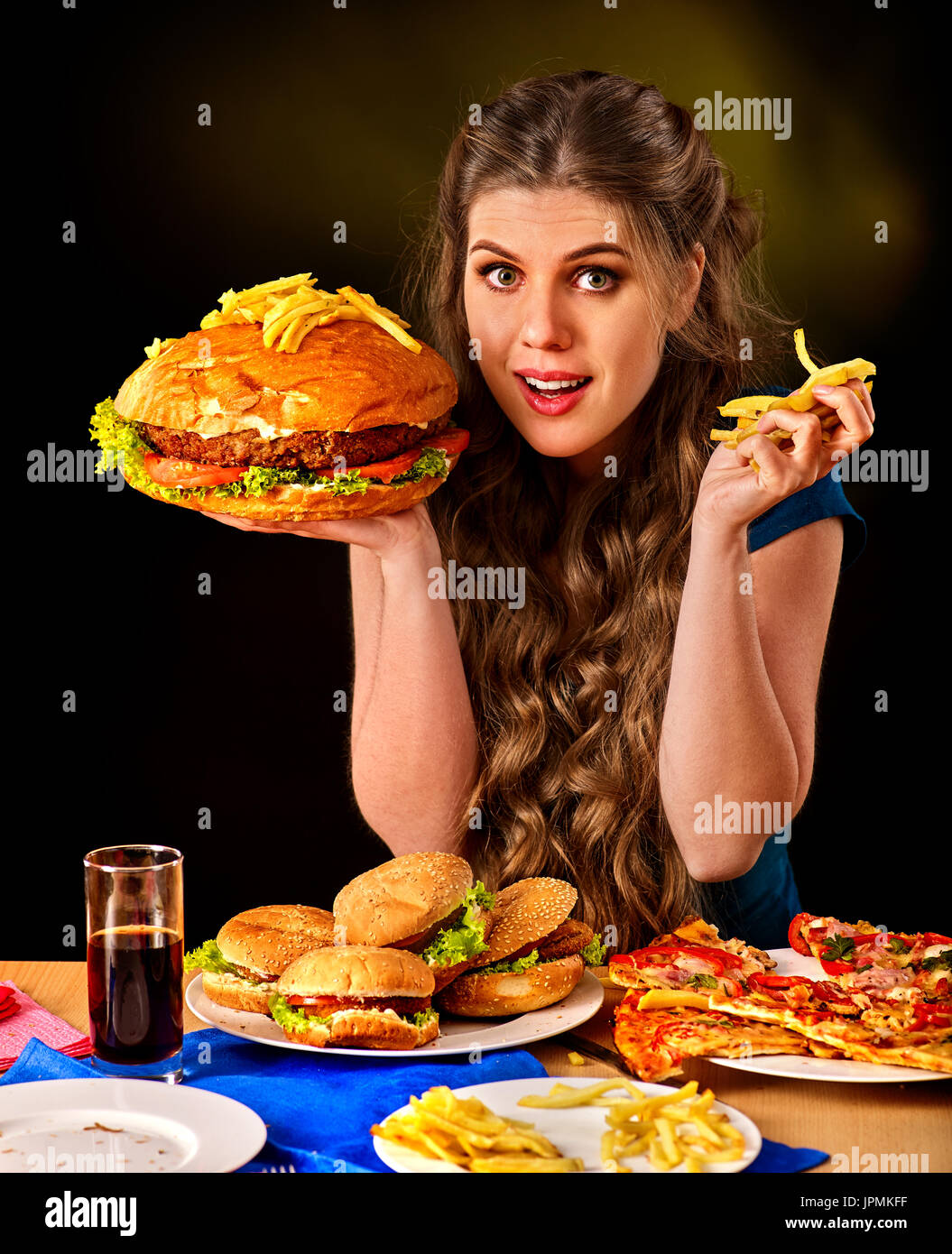 Donna di mangiare patatine e hamburger sul tavolo. Foto Stock