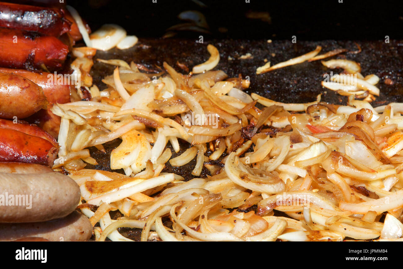 Salsicce e salami, hot dogs e cipolle grigliare su una griglia aperta. Foto Stock