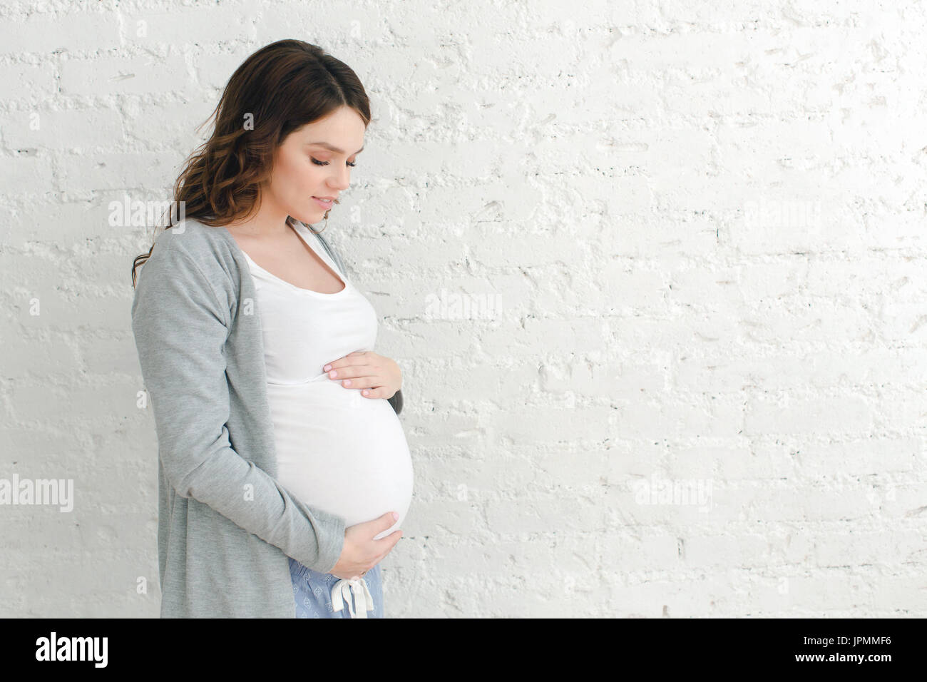 Donna incinta toccando ventre su sfondo bianco Foto Stock