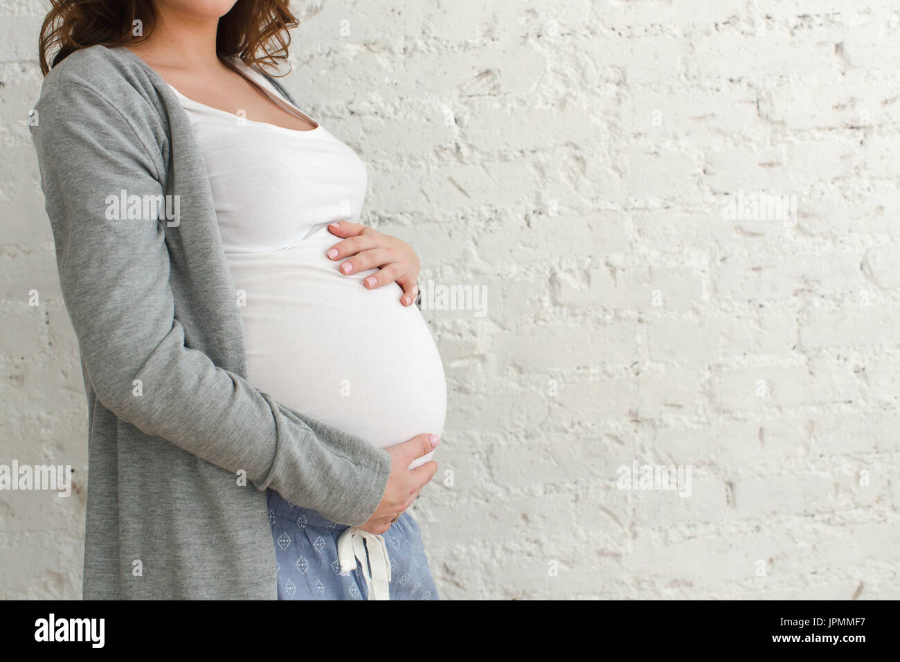 Donna incinta toccando ventre close-up su sfondo bianco Foto Stock